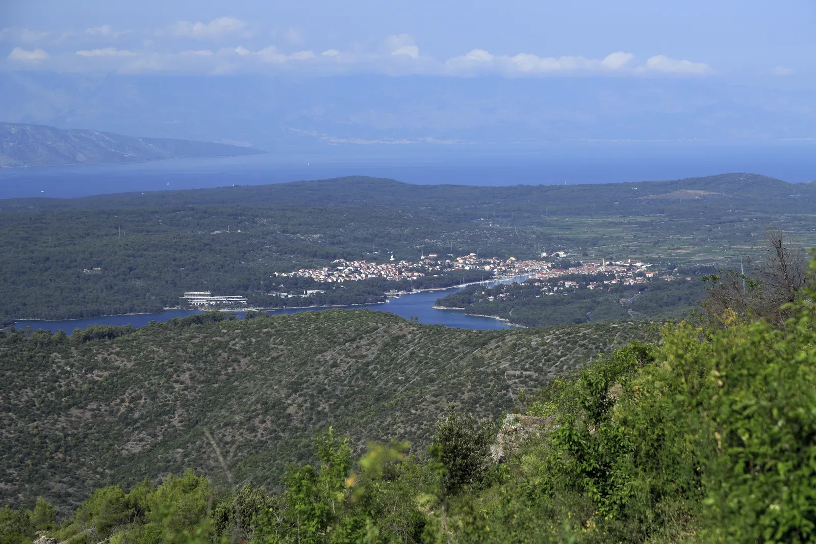 vista desde lo alto de la isla de hvar: la ensenada larga y estrecha que lleva al puerto de stari grad, la antigua faros, con el pueblo al fondo de la bahía, colinas de monte bajo en primer plano y, detrás, el mar y las montañas de la costa