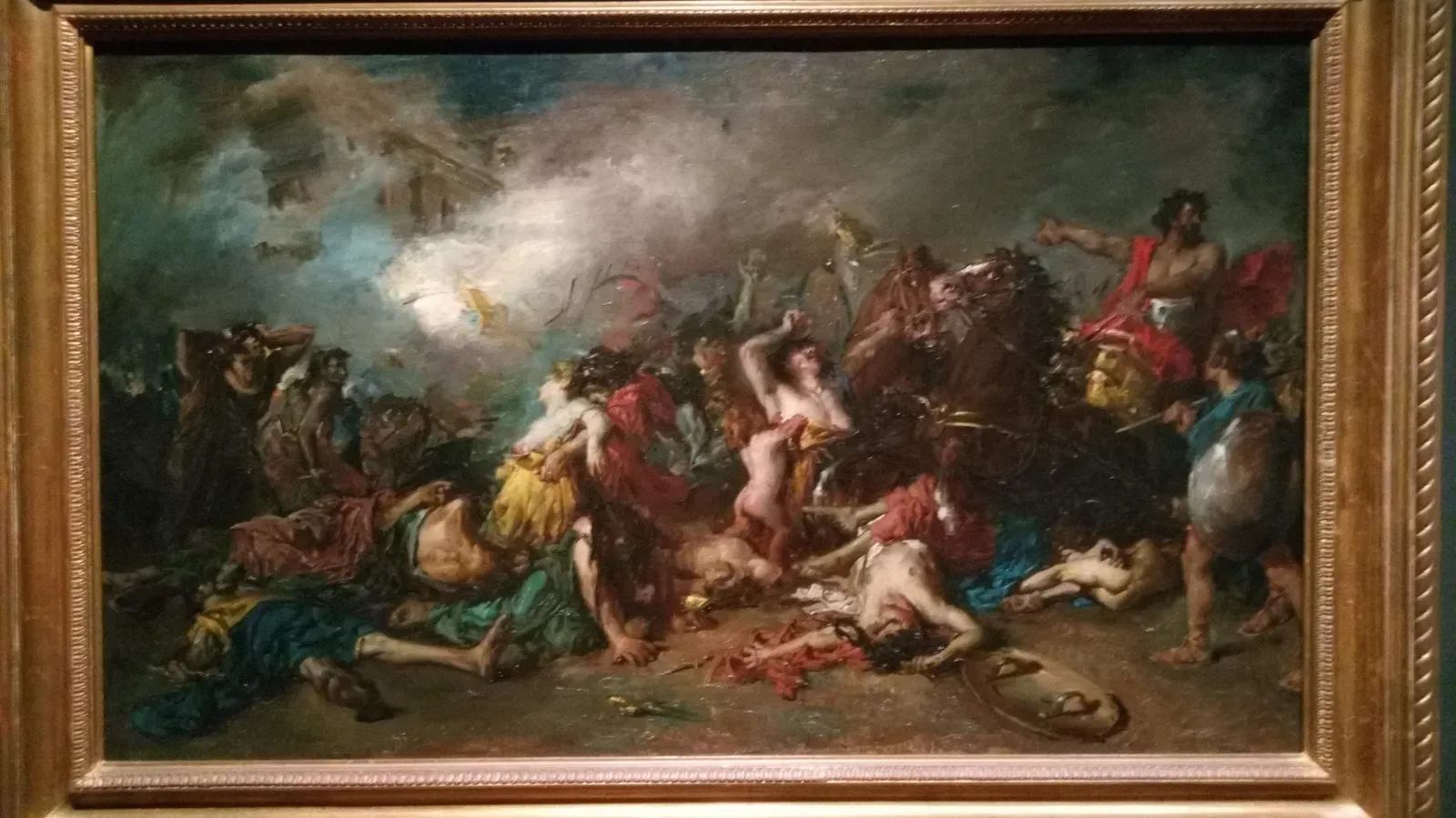 pintura de historia del siglo xix en su marco dorado: cuerpos caídos y mujeres que se desploman entre el humo, a la derecha un guerrero barbudo a caballo que señala con el brazo extendido y, al fondo, edificios envueltos en humo