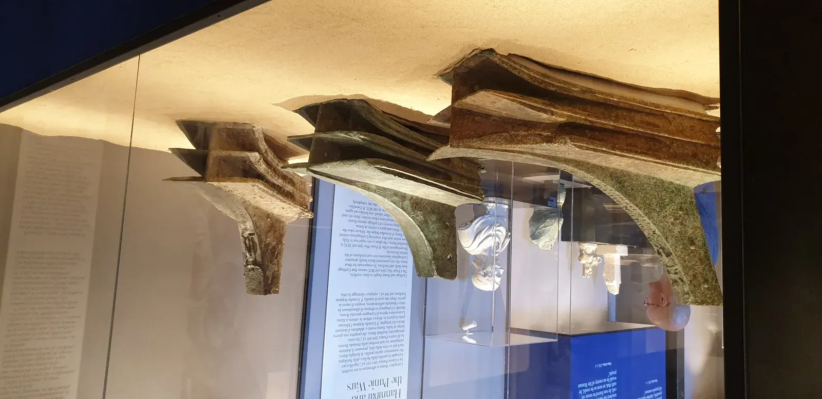 tres arietes de bronce recuperados del fondo de las egadas, montados en fila dentro de una vitrina iluminada