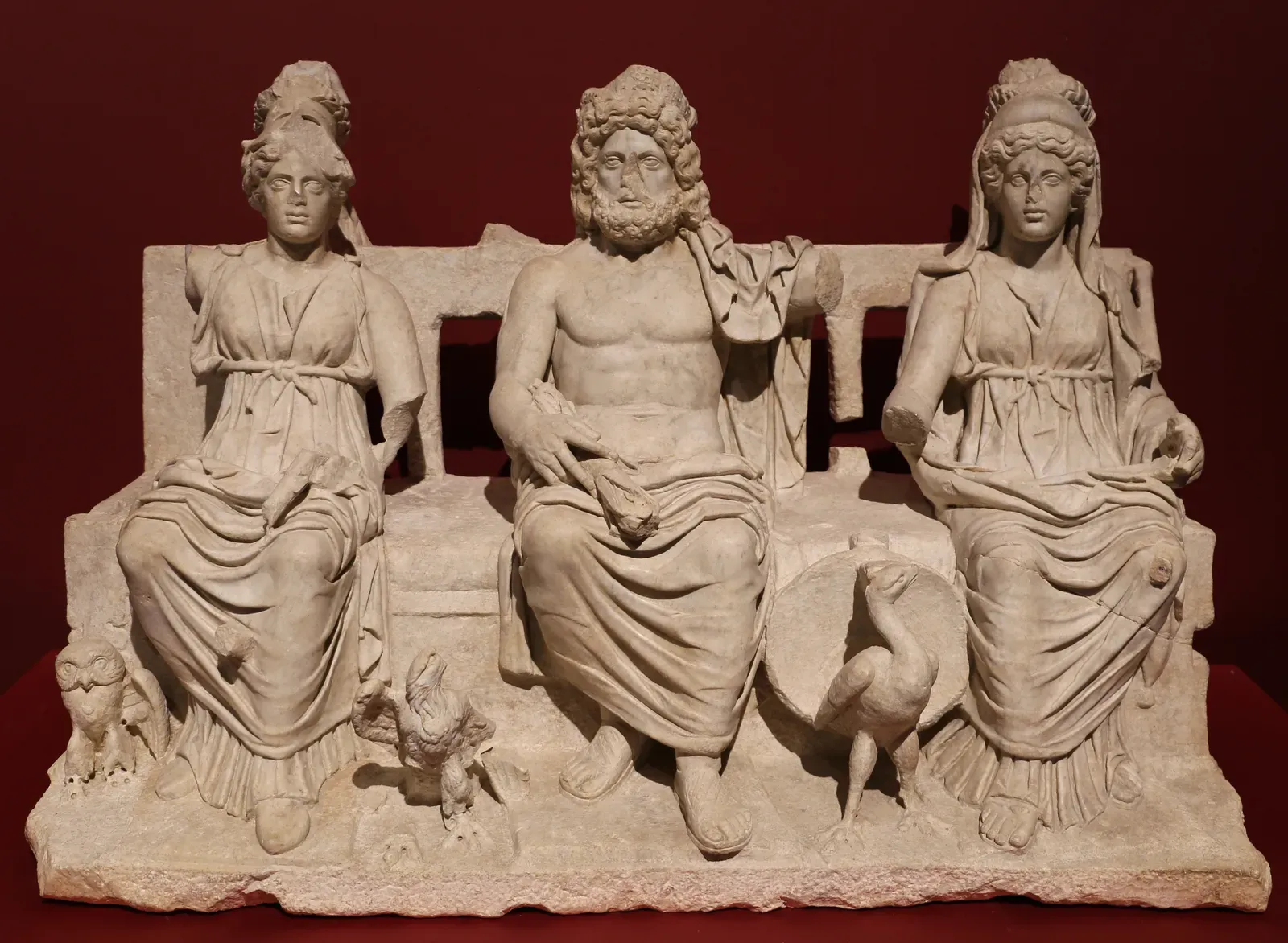 la tríada capitolina en mármol: júpiter entronizado en el centro, con minerva a un lado y juno al otro y sus animales a los pies
